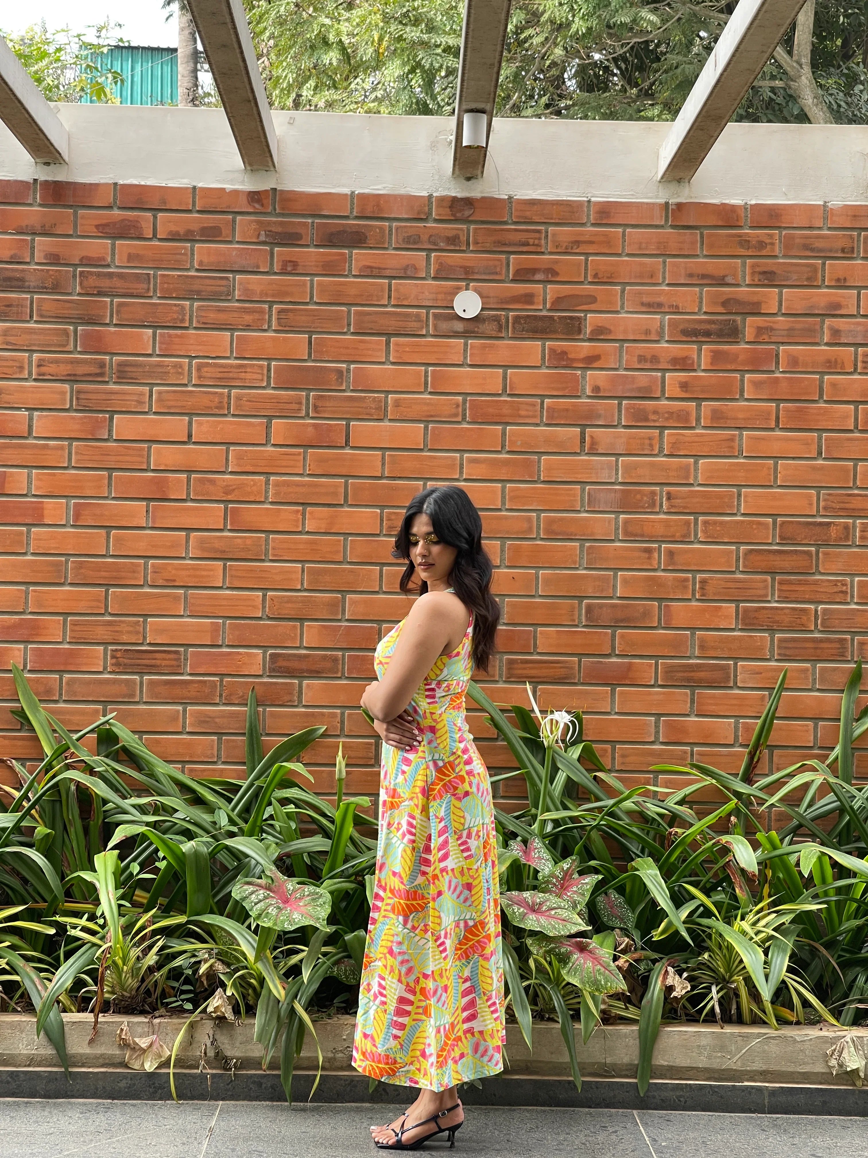 Woman in a colorful dress standing on a brick patio with plants around.