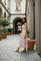 Woman in a floral dress standing in an outdoor courtyard with potted plants and architectural elements.